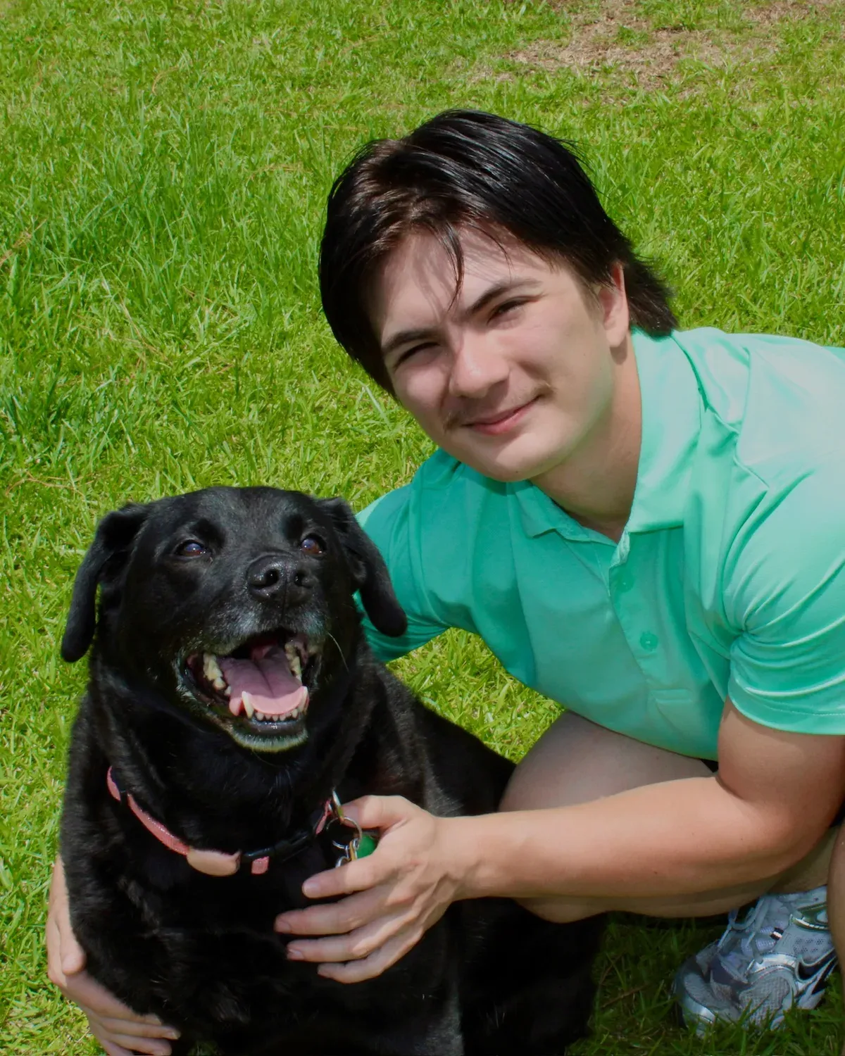 Ethan crouching next to a happy black Labrador in a grassy backyard