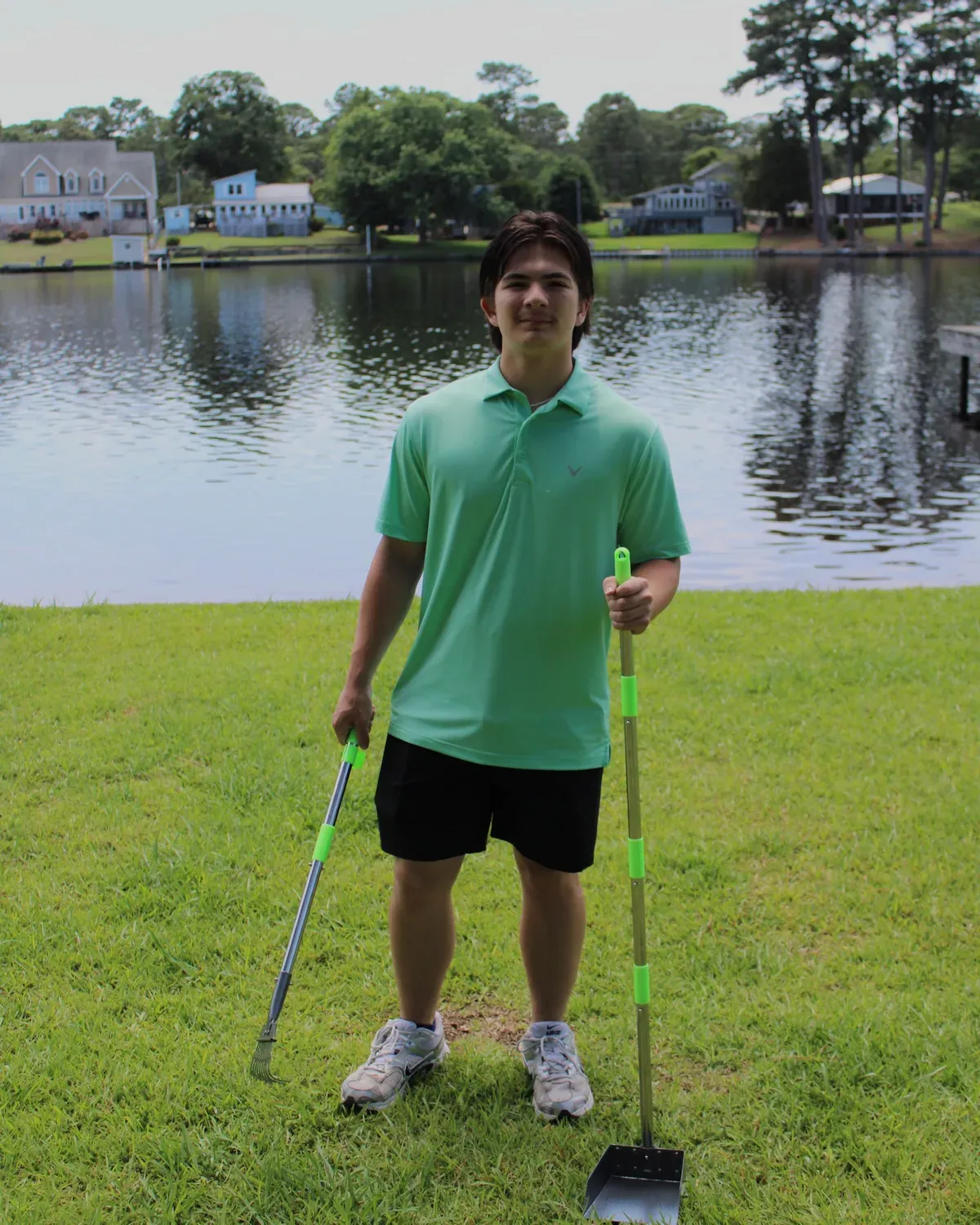 Ethan, owner of Waggintails Waste Solutions, holding pooper-scooper tools by a lake in Goldsboro, NC